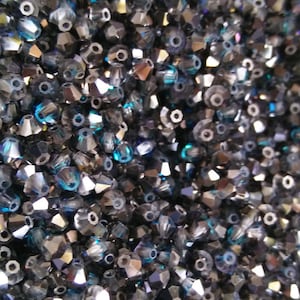 May include: A close-up of a large quantity of dark blue and silver crystal beads. The beads are faceted and have a shiny finish.