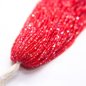 May include: A strand of red seed beads with a white tassel. The beads are small and have a slight iridescent sheen.