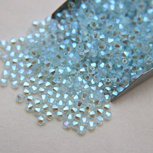 May include: A large quantity of light blue iridescent glass beads. The beads are small and have a faceted, round shape.