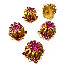 Può includere: Cinque bottoni vintage in metallo dorato con strass rosa acceso. I bottoni hanno un design floreale con uno strass centrale circondato da pietre più piccole. I bottoni sono su sfondo bianco.