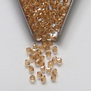 Peut inclure: Gros plan sur un petit tas de perles en verre brun clair. Les perles sont facettées et ont une finition brillante. Les perles se déversent d'un récipient en métal.