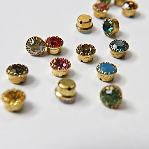May include: Assortment of colorful rhinestones with gold settings. The rhinestones are in various colors, including red, blue, green, and clear.