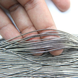 Puede incluir: Primer plano de un haz de alambre de color plateado. El alambre es delgado y flexible, y está dispuesto en una pila ordenada.