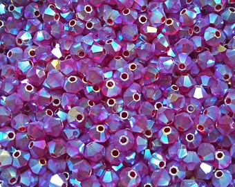 May include: A close-up view of a large quantity of small, faceted, iridescent purple glass beads. The beads have a metallic sheen and are perfect for jewelry making.