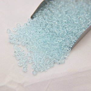 May include: A scoop of light blue glass beads. The beads are small and round, and they have a slight sparkle to them.