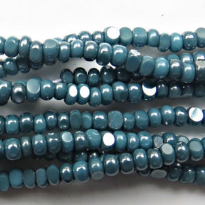 May include: A strand of teal blue glass seed beads. The beads are small and round, with a slightly iridescent finish.
