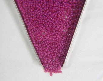 May include: A close-up of a metal funnel filled with small, pink, round beads. The beads are spilling out of the funnel onto a white surface.