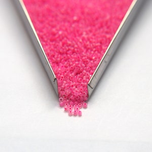 Op de afbeelding: Een metalen bak gevuld met roze zaadkraaltjes die op een wit oppervlak vallen.