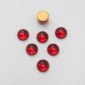 Puede incluir: Seis cabujones redondos de vidrio rojo con superficie reflectante. Un cabujón tiene un reverso beige, los otros tienen un reverso oscuro. Estas piezas decorativas de vidrio son adecuadas para la fabricación de joyas y manualidades.