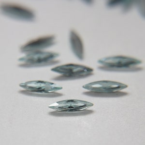 Puede incluir: Un grupo de piedras preciosas de forma marquesa azul claro esparcidas sobre una superficie blanca.