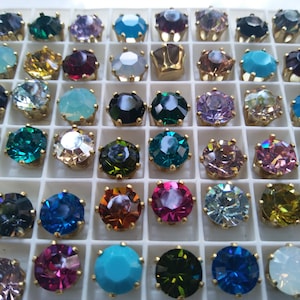 May include: Assortment of colourful round rhinestones in a white gridded display case. The rhinestones are arranged in rows and columns, with each rhinestone having a different colour and design.