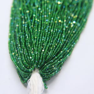 May include: A strand of green glass seed beads with a sparkly finish. The beads are strung on a white thread.