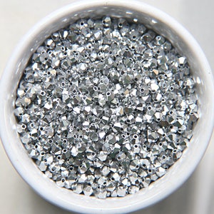 May include: A bowl filled with silver-colored faceted glass beads. The beads are small and have a shiny, reflective surface.