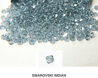 Könnte beinhalten: Nahaufnahme eines Haufens kleiner, hellblauer, facettierter Glasperlen. Die Perlen sind alle gleich groß und gleich geformt und in einem zufälligen Muster angeordnet. Die Perlen sind mit "Swarovski Indian Sapphire" beschriftet.