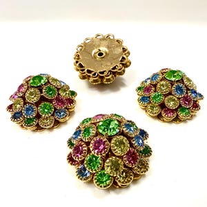 Può includere: Quattro orecchini vintage color oro con strass colorati. Gli orecchini sono rotondi e presentano un gruppo di pietre verdi, blu, rosa e gialle. Un orecchino è mostrato dal retro, rivelando il perno.