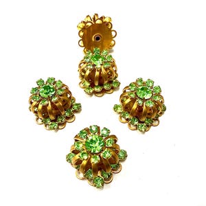 Può includere: Quattro orecchini vintage in metallo color oro con accenti di strass verde brillante. Gli orecchini hanno un design floreale con una pietra verde centrale circondata da pietre verdi più piccole. Su sfondo bianco.