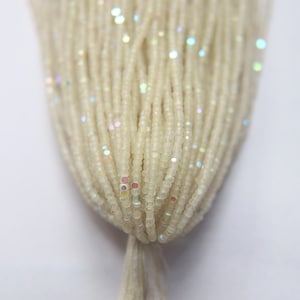 May include: A strand of white iridescent seed beads. The beads are small and round, with a slight shimmer.
