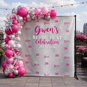 May include: A retirement celebration backdrop with the text "Gwen's Retirement Celebration 39 Years" in pink. The backdrop is silver and white, decorated with pink and silver balloons and star-shaped decorations.