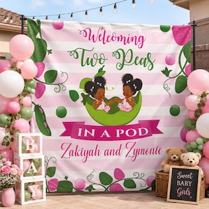May include: A baby shower backdrop with pink and white stripes, featuring the text "Welcoming Two Peas In A Pod" and the names Zakiyah and Zymonie. The backdrop includes illustrations of two babies in a pea pod, balloons, and decorative elements.