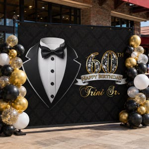 May include: A black backdrop with a tuxedo graphic and gold text that reads "60th Happy Birthday Trini Jr." The backdrop is decorated with black, gold, and white balloons. The tuxedo graphic includes a black bow tie and buttons.