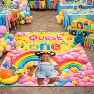 May include: A colorful birthday party scene with a young child standing on a vibrant mat. The mat features a rainbow, musical notes, and the text "Quest turns ONE." Balloons, a toy bus, and other party decorations are visible.