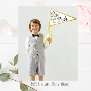 May include: A young person in a gray pinstripe vest and shorts holds a triangular flag with gold trim and the words "Here Comes the Bride" in black script. The flag has yellow ribbons attached. The image has a soft, light background.