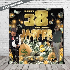 Puede incluir: Un telón de fondo negro con un diseño dorado de "Happy 38th Birthday Jasper". El diseño incluye símbolos de dólar dorados, sacos de dinero y montones de efectivo. Dos personas están de pie a ambos lados del telón de fondo.
