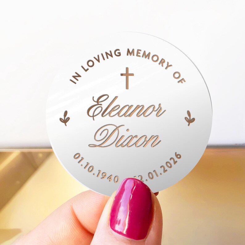 May include: A round, white memorial sticker with the text "IN LOVING MEMORY OF Eleanor Dixon" and dates 01.10.1940 - 02.01.2026. The design includes a cross and floral accents in a copper color.