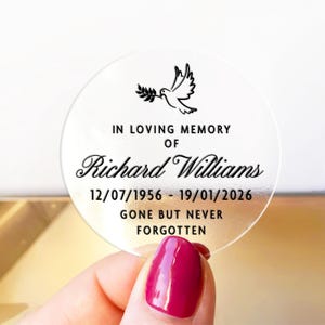 May include: A clear, round memorial sticker with black text and a dove illustration. The text reads "IN LOVING MEMORY OF Richard Williams 12/07/1956 - 19/01/2026 GONE BUT NEVER FORGOTTEN."