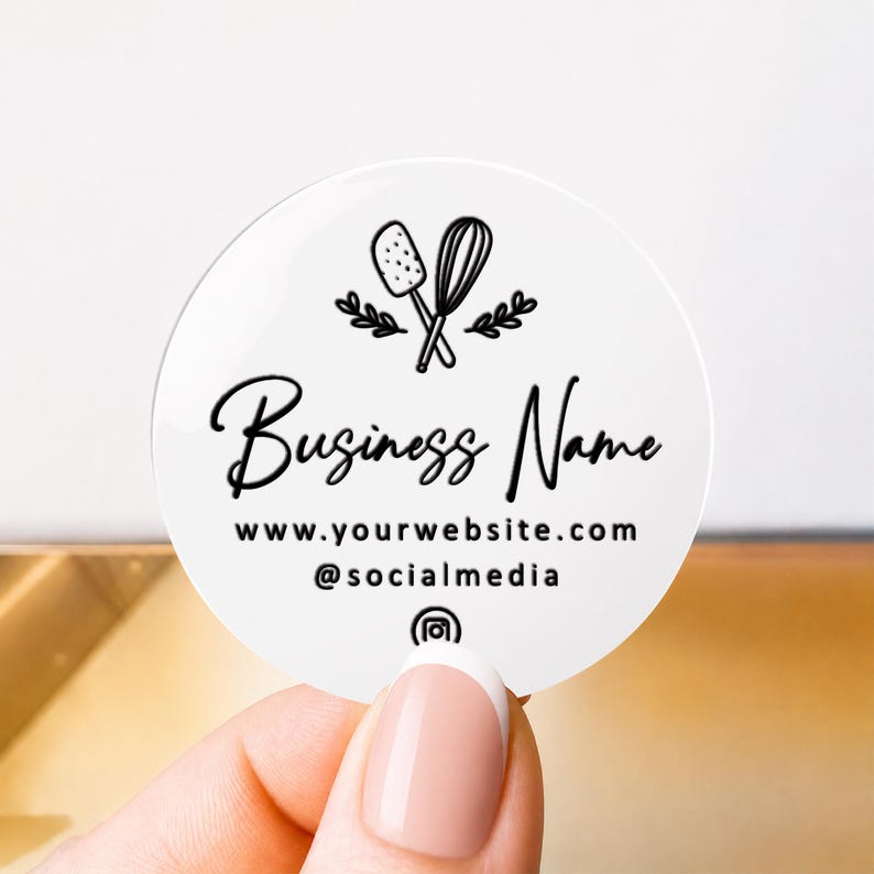 Pu&ograve; includere: Un adesivo circolare bianco con un disegno a linee nere di una spatola e una frusta con rametti di foglie. Il testo recita Business Name, www.yourwebsite.com e @socialmedia, accompagnato da una piccola icona di Instagram al centro in basso.