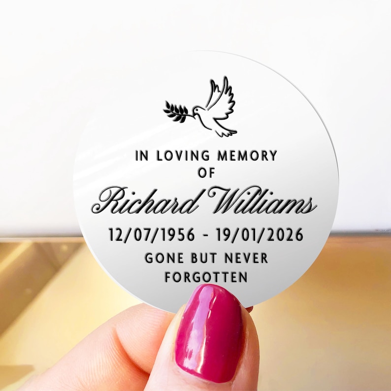 May include: A round, white memorial sticker with black text and a dove illustration. The text reads "IN LOVING MEMORY OF Richard Williams 12/07/1956 - 19/01/2026 GONE BUT NEVER FORGOTTEN". The sticker is held by a hand with a red nail polish.