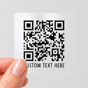 May include: A square, transparent sticker featuring a black and white QR code pattern. Below the QR code, the text CUSTOM TEXT HERE is printed in a clean, sans-serif font. The sticker has a smooth, semi-gloss finish and rounded corners.