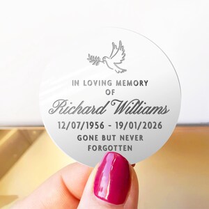 May include: A round, white memorial keepsake with the text "IN LOVING MEMORY OF Richard Williams 12/07/1956 - 19/01/2026 GONE BUT NEVER FORGOTTEN." A dove with an olive branch is at the top.