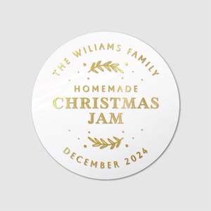 Op de afbeelding: Ronde witte sticker met gouden tekst die "The Williams Family Homemade Christmas Jam December 2024" luidt. De tekst wordt omringd door een gouden hulsttak.