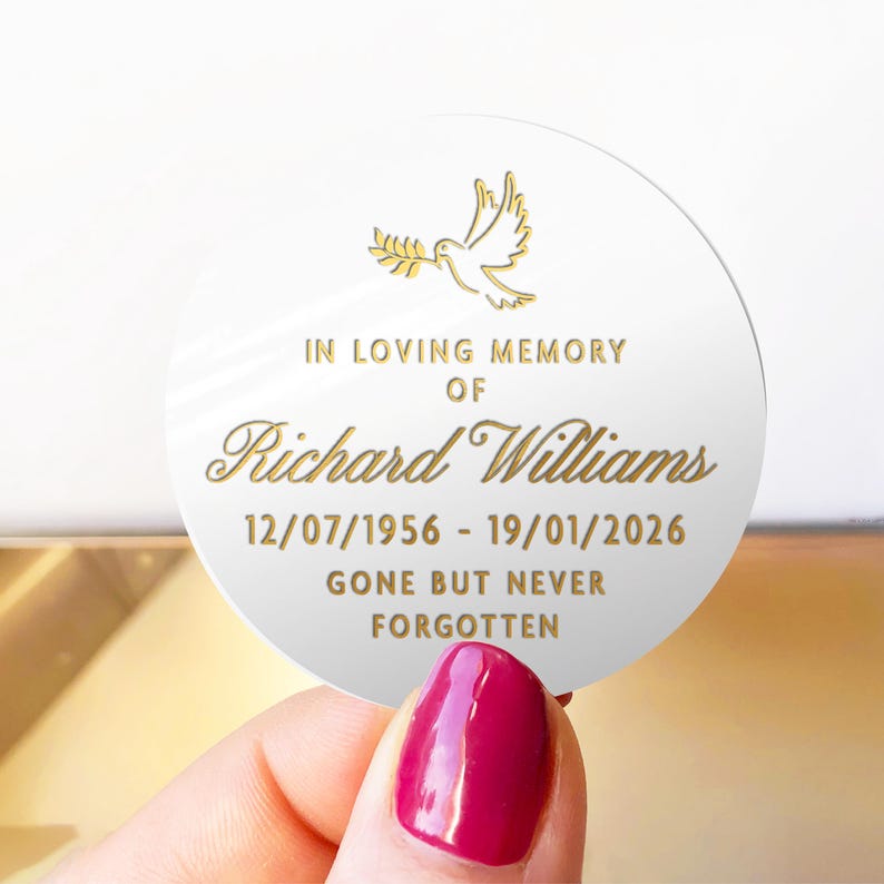 May include: A white, round memorial keepsake with gold text and a dove illustration. The text reads "IN LOVING MEMORY OF Richard Williams 12/07/1956 - 19/01/2026 GONE BUT NEVER FORGOTTEN."