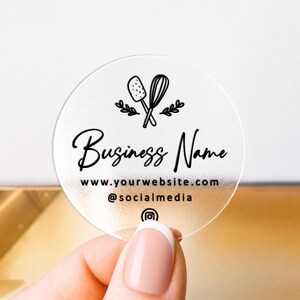 Pu&ograve; includere: Un adesivo circolare, satinato e semitrasparente, con un disegno a linee nere di una spatola e una frusta incrociate con rametti. Il testo riporta Business Name, www.yourwebsite.com, @socialmedia, e include un'icona di Instagram.