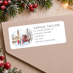 May include: A rectangular address label featuring a watercolour illustration of a snowy London street with Big Ben, a red double-decker bus, and people in winter coats. The text reads: SOPHIE TAYLOR, 10 UPPER BANK ST, CANARY WHARF, LONDON, E14 5NP, UNITED KINGDOM.