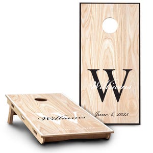 May include: Two rectangular cornhole boards with a light wood grain finish. Each board features a circular hole at the top, a large black letter W, the name Williams in script, and the date June 8, 2025, printed on the surface of the wood.