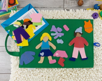 May include: A green felt play mat with two felt figures, one with a blue dress and one with a red jacket. The figures have various clothing pieces that can be mixed and matched. The mat has a blue felt pocket on the side.