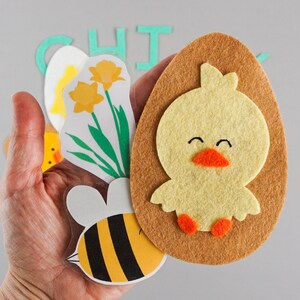 Cute felt chick on felt egg in hand with laminated bee and daffodils.