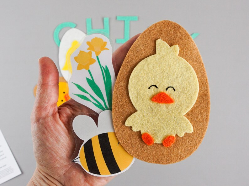 Cute felt chick on felt egg in hand with laminated bee and daffodils.