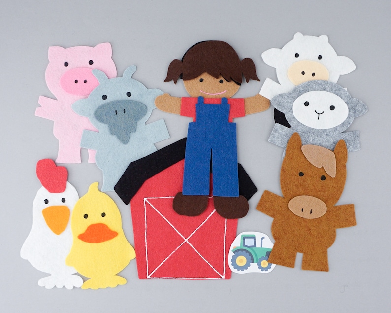 May include: Felt farm animal figures, including a pig, cow, sheep, horse, and a girl wearing overalls. The figures are standing in front of a red barn with a white X on the front. There is also a yellow chick and a tractor.
