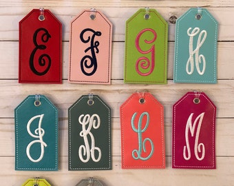 May include: A collection of personalized gift tags in various colors, each featuring a different embroidered letter in a cursive font. The tags are in shades of peach, teal, green, black, red, pink, lime green, and gray.