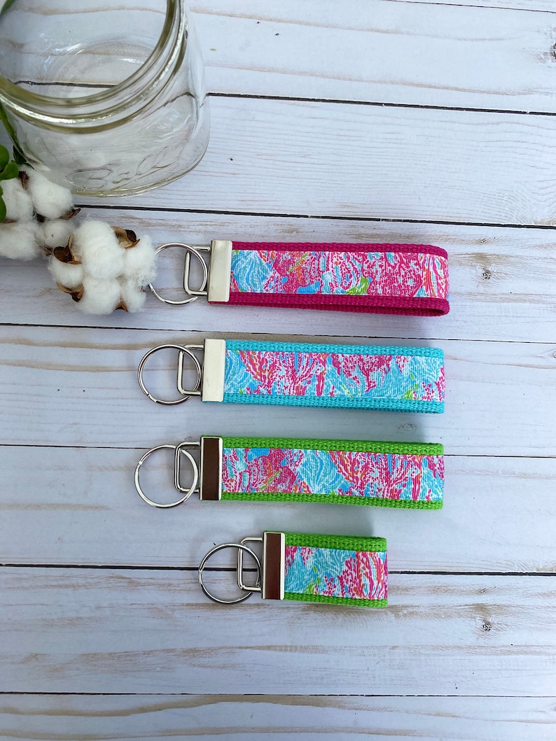 Puede incluir: Cuatro llaveros con anillas de plata y correas de tela con estampados coloridos. Las correas presentan un dise&ntilde;o floral rosa, azul y verde.