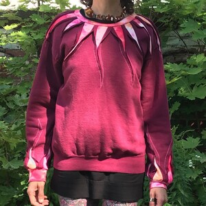 Könnte beinhalten: Ein maroonfarbener Pullover mit einem pink- und weißfarbenen Tie-Dye-Muster an Ausschnitt und Ärmeln. Der Pullover hat eine lockere Passform und einen Rundhalsausschnitt.
