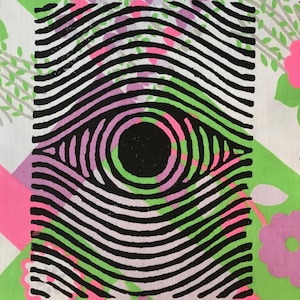 Könnte beinhalten: Stoffmuster mit einem schwarz-weißen Augendesign mit konzentrischen Kreisen. Das Auge ist vor einem Hintergrund aus rosa, grünen und weißen Blumenmustern platziert. Die Kanten des Stoffes sind gezackt.