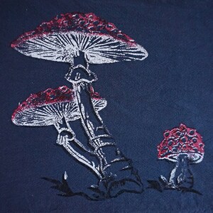 Peut inclure: Une illustration de champignon blanc et rouge sur un fond bleu foncé. Le champignon a un pied blanc et un chapeau rouge avec des points blancs. Il y a deux champignons plus petits en arrière-plan.