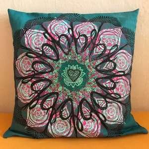May include: Teal blue throw pillow with a black and white mandala design. The mandala features a pink and white floral pattern with a black outline. The center of the mandala has a green and black lotus flower.