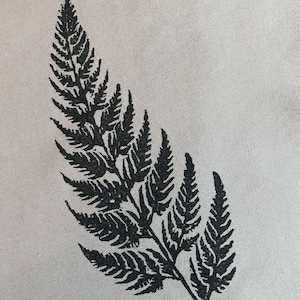 May include: A black fern leaf design printed on a light grey fabric. The fern's detailed with many small leaflets, creating a textured appearance. The image is a close-up, showing the intricate details of the plant.