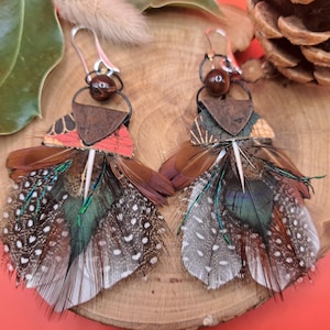 Op de afbeelding: Een paar veren oorbellen met een bruin, rood en groen kleurenschema. De oorbellen zijn gemaakt met verschillende veren, waaronder fazantenveren, en zijn versierd met een bruin lederen en kurk stuk.